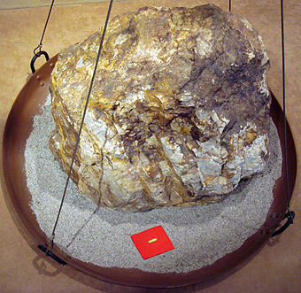 Een 860kg blok gouderts met daarvoor op 
een rood kartonnetje 30g goud dat daaruit
kan worden gewonnen. Toi goudmijn, Japan 
PHGCOM 2007 en.wikipedia.org